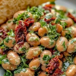Bowl of marinated sun-dried tomato bean salad garnished with fresh herbs