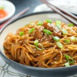Bowl of teriyaki noodles with vegetables, garnished with sesame seeds and green onions