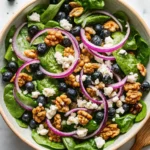Fresh blueberry walnut salad with greens, cheese, and vinaigrette in a white bowl