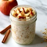 Bowl of chilled apple cinnamon oatmeal topped with fresh apple slices and a sprinkle of cinnamon