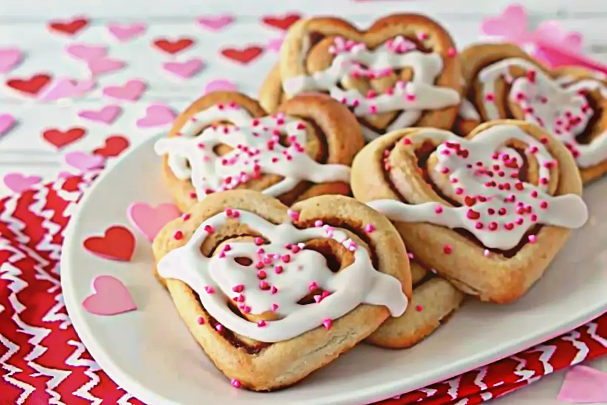 Sweetheart cinnamon rolls arranged in a heart-shaped pan with pink icing and Valentine sprinkles.