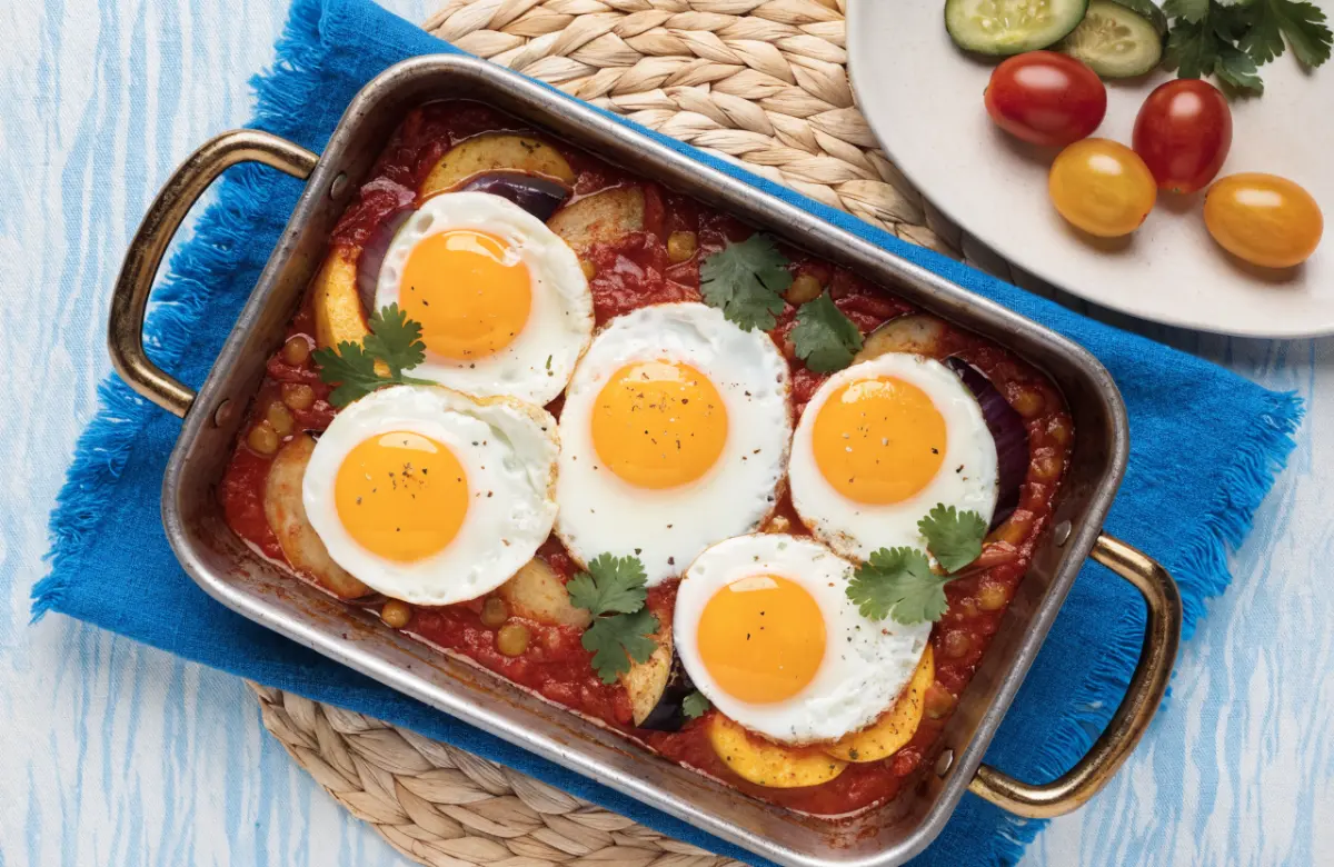 Shakshuka traybake recipe with baked eggs, roasted peppers, tomatoes, and fresh herbs