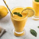 Refreshing mango lemonade recipe in a glass with ice, fresh mango, lemon slices, and mint leaves.