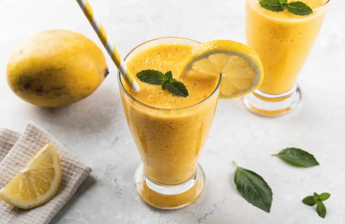 Refreshing mango lemonade recipe in a glass with ice, fresh mango, lemon slices, and mint leaves.